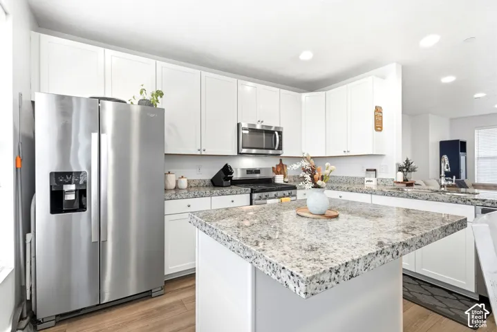 White cabinetry, stainless steel appliances, wood-finish flooring, granite countertops, and recessed lighting