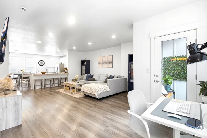 Open-concept living space with wood-finish flooring, a kitchen island with seating, recessed lighting, and a glass-paneled door