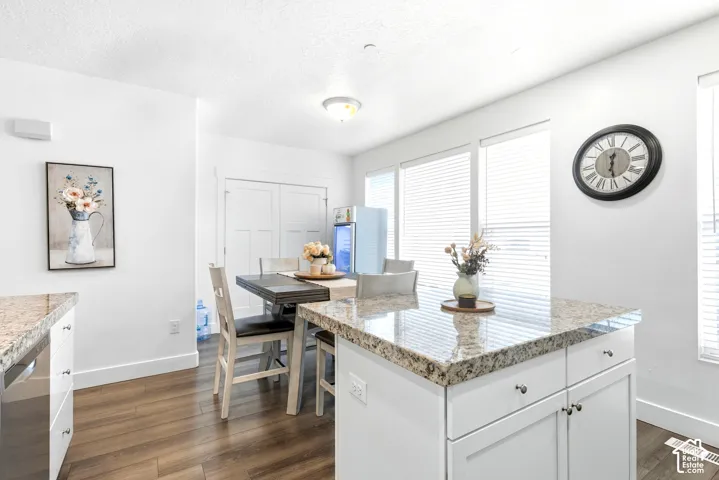 White kitchen island with granite-finish countertop, wood-finish flooring, and white cabinetry