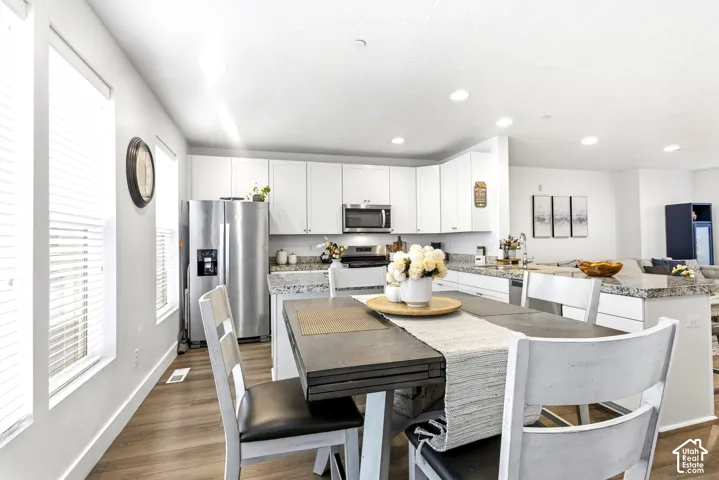 Kitchen featuring white cabinetry, stainless steel appliances, granite-style countertops, wood-finish flooring, and recessed lighting