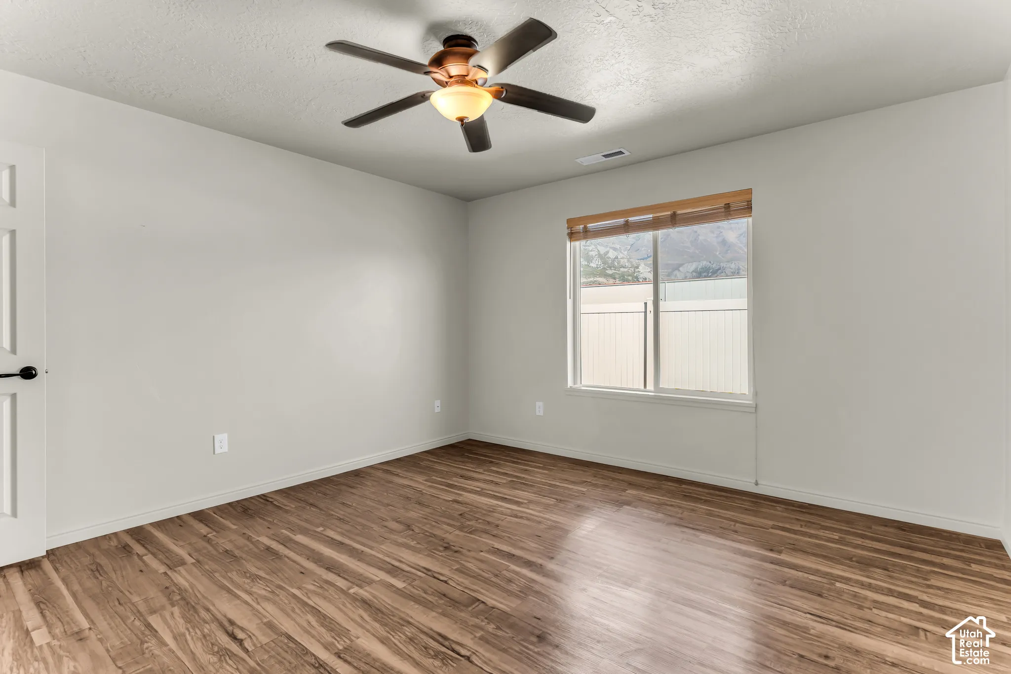 Wood-finish flooring, ceiling fan with integrated lighting, and a single window with mountain scenery