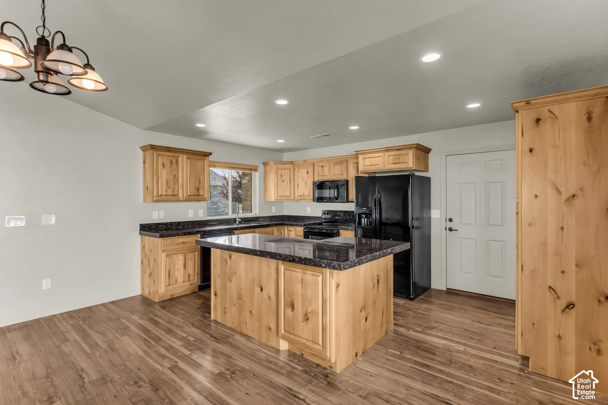 Spacious kitchen featuring wood-finish cabinetry, dark countertops, black appliances, and recessed lighting