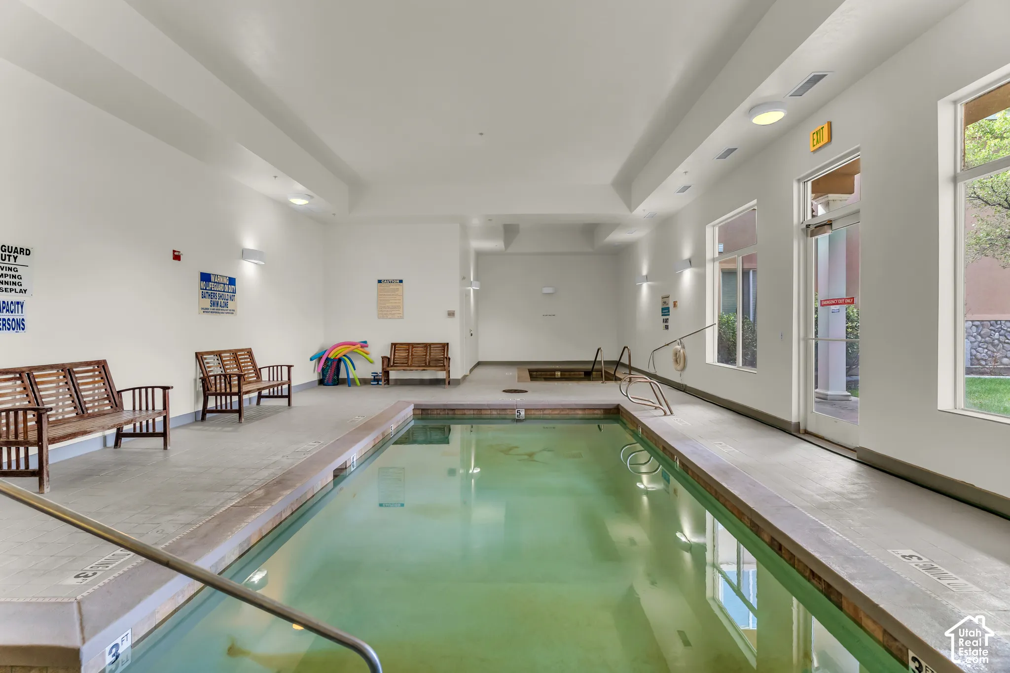 Indoor swimming pool with integrated spa, concrete deck, and transom windows
