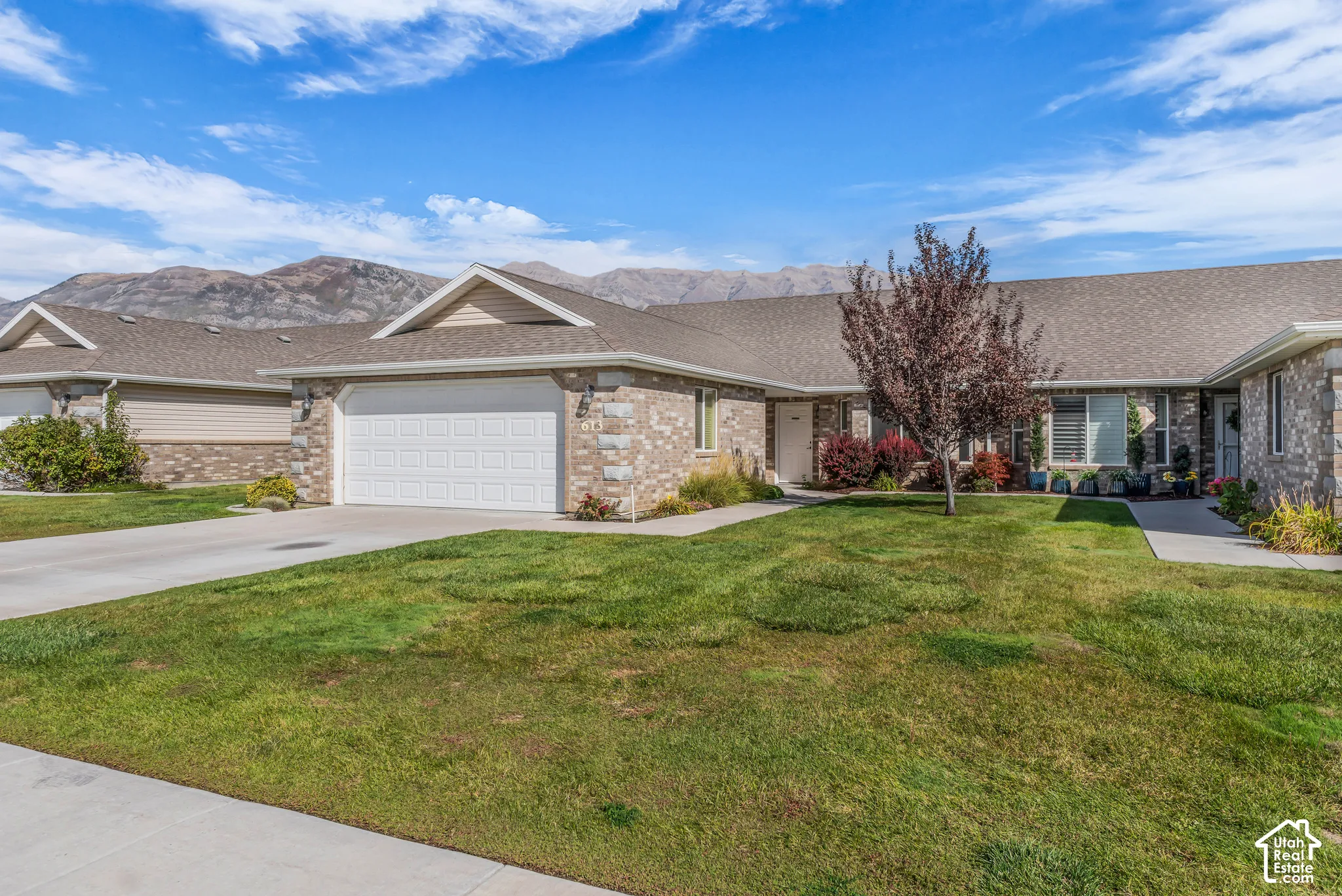 Brick exterior with an attached garage, featuring a paved driveway and concrete pathways
