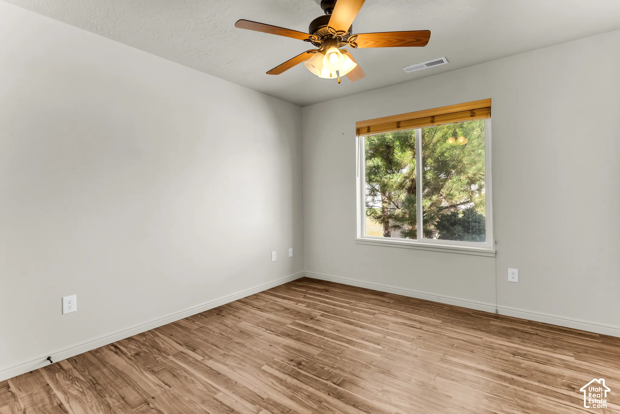 Wood-finish flooring, ceiling fan with integrated lighting, and a window with wood-finish blinds