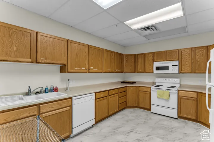 Extensive wood-finish cabinetry, white dual basin sink, white dishwasher, white electric range with overhead microwave, and light-toned countertops