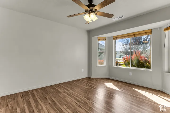 Wood-finish flooring throughout, bay window with multiple panes, ceiling fan light fixture, and light neutral wall colors