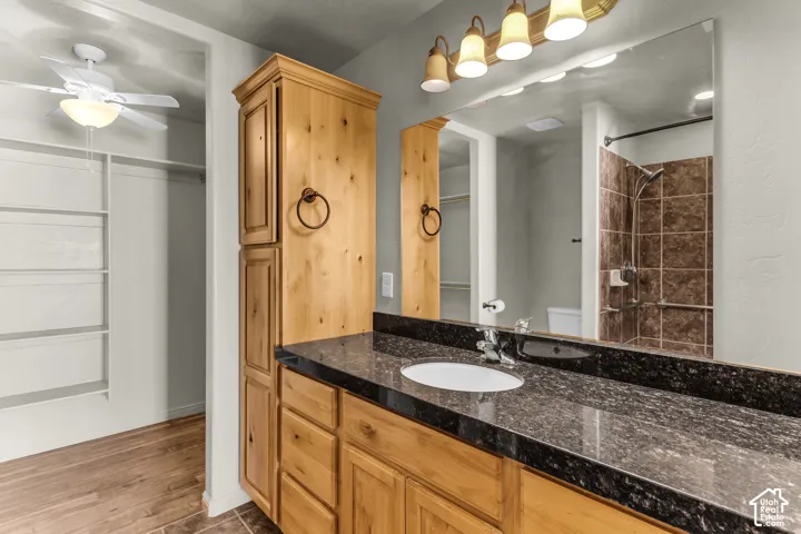 Wood-finish flooring, built-in storage shelving, wood cabinetry, dark speckled countertop, and tiled shower surround