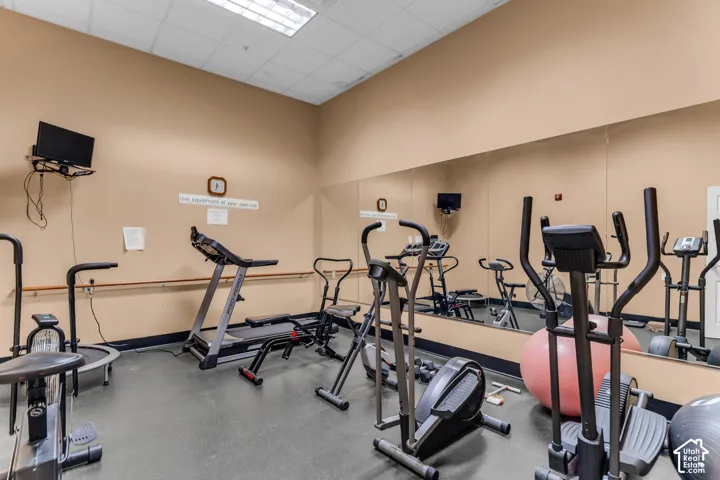 Fitness area featuring cushioned flooring, full-wall mirrors, and track lighting