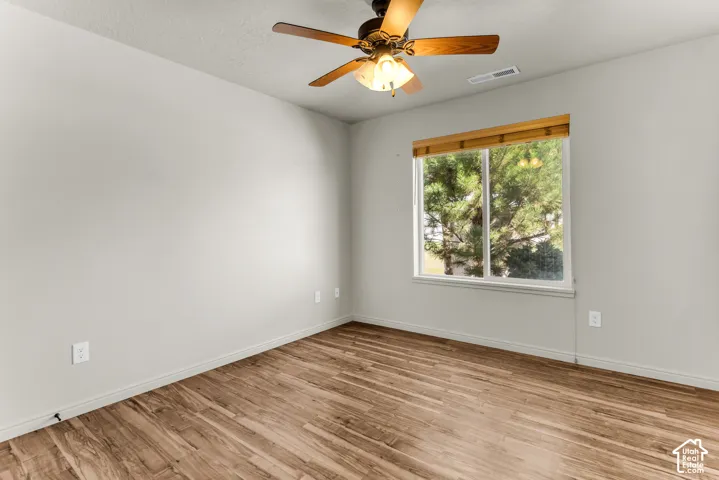 Wood-finish flooring, ceiling fan with integrated lighting, and a window with wood-finish blinds
