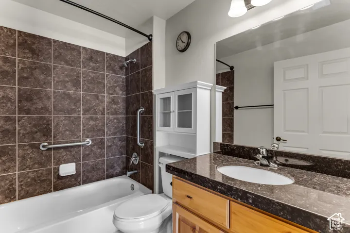 Tiled tub/shower combination with grab bars, wood-finish vanity with an integrated sink, and a large wall-mounted mirror