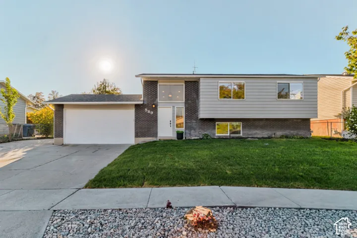 Split-level residence featuring a two-car garage, brick and siding exterior, front lawn, and mature landscaping