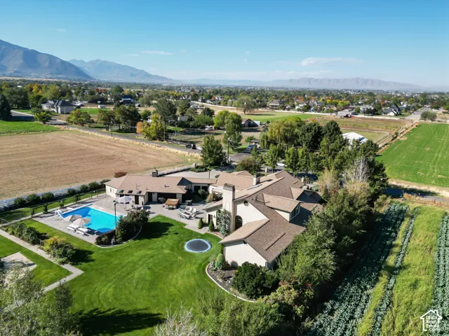 Aerial perspective of property featuring an expansive lawn, in-ground swimming pool, masonry chimney, and established mature trees, set against a backdrop of mountain ranges