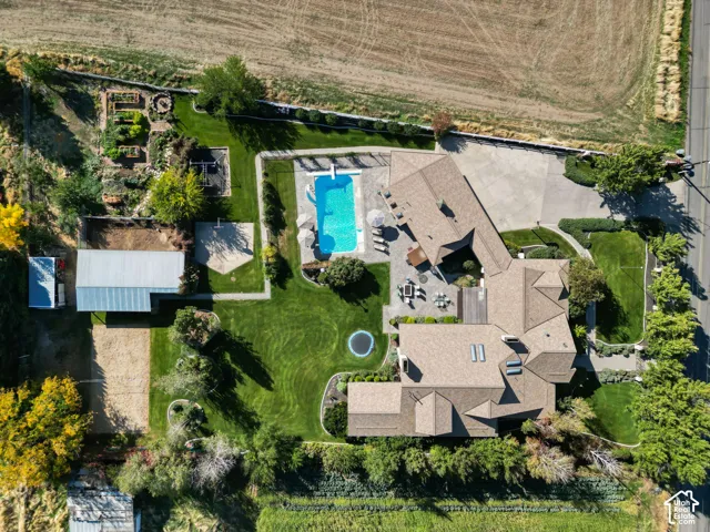 Aerial view featuring an expansive lot with an in-ground swimming pool, stone-paver patio, detached accessory building, and manicured lawn