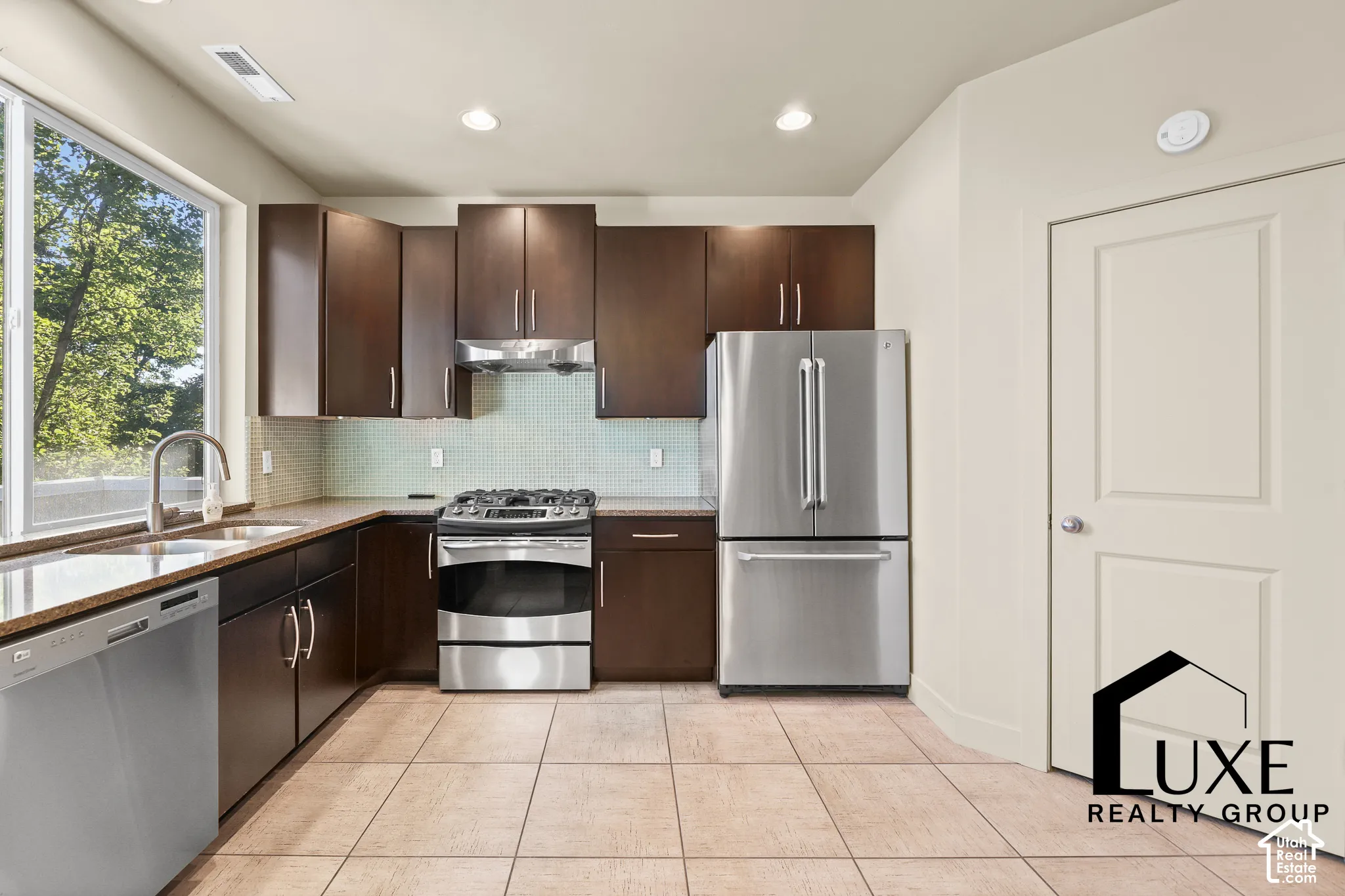 Modern kitchen featuring dark wood-finish cabinetry, stainless steel appliances, granite countertops, and a tile backsplash