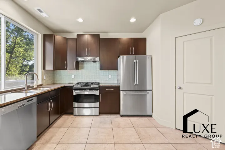 Modern kitchen featuring dark wood-finish cabinetry, stainless steel appliances, granite countertops, and a tile backsplash