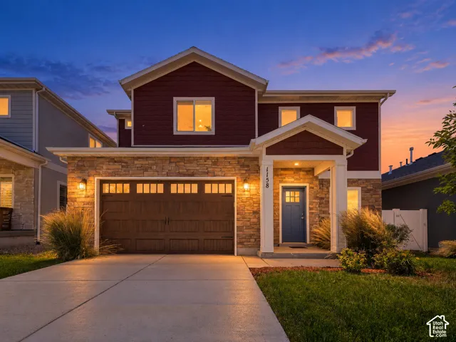 Stone veneer and siding exterior with an attached garage, covered front entry, concrete driveway, and front landscaping