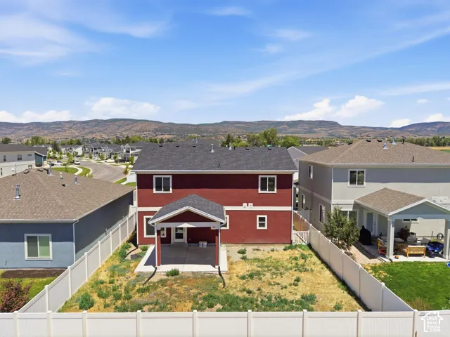 Red exterior with white trim, dark asphalt shingle roof, rear covered patio, white vinyl fencing, and mountain backdrop