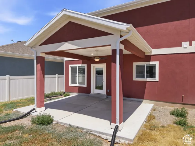 Covered patio with an exterior ceiling fan, stucco exterior, and white vinyl fencing
