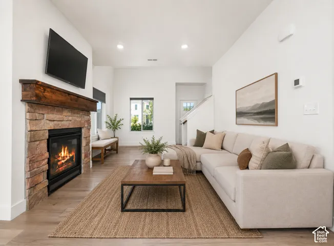 Stone-faced fireplace with a wood mantel, wood-finish flooring, recessed lighting, and a prominent staircase