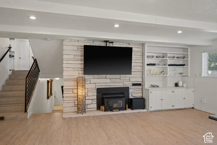 Stone-clad fireplace with wood-finish hearth, recessed lighting, wood-finish flooring, built-in shelving, and built-in cabinetry