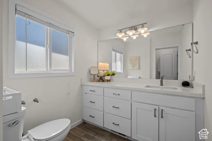 White vanity with a light-colored countertop and integrated sink, under-mount cabinetry, and wood-finish flooring
