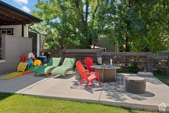 Expansive concrete patio with a fire pit table, surrounded by a decorative block wall and mature trees