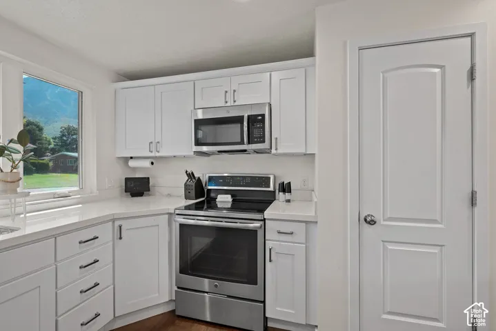 White shaker-style cabinetry with dark hardware, stainless steel appliances, light-toned countertops, and wood-finish flooring