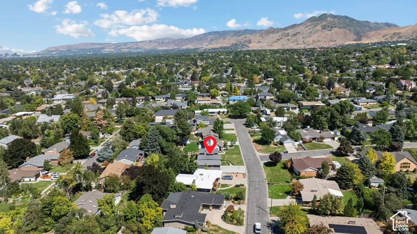 Aerial view showcasing a residential neighborhood featuring tree-lined streets, mature landscaping throughout the community, and mountain backdrop