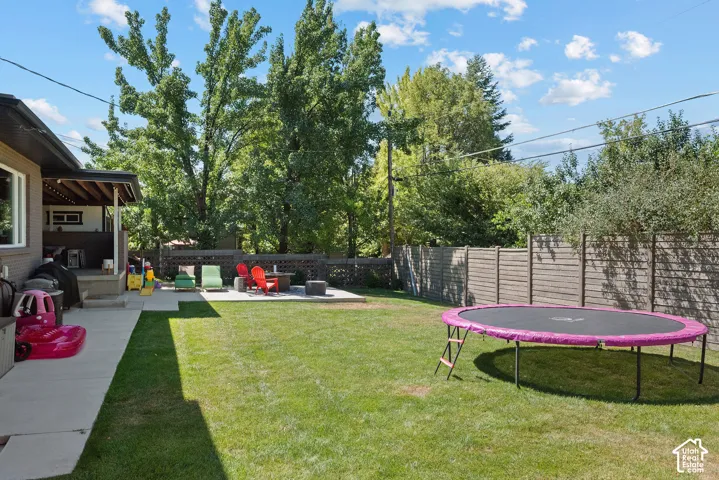Expansive backyard featuring a lush lawn, mature trees, a privacy fence, and a concrete patio