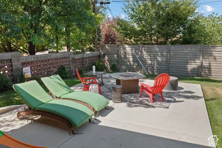 Expansive concrete patio with a fire pit, bordered by a decorative block wall and a privacy fence, surrounded by green lawn and mature trees