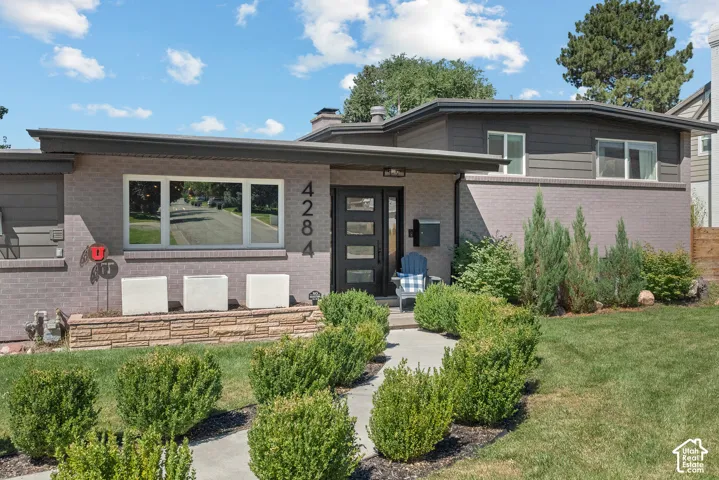 Contemporary exterior featuring brick and horizontal siding, a flat roofline, a modern front door with vertical panels, and established landscaping with a concrete walkway