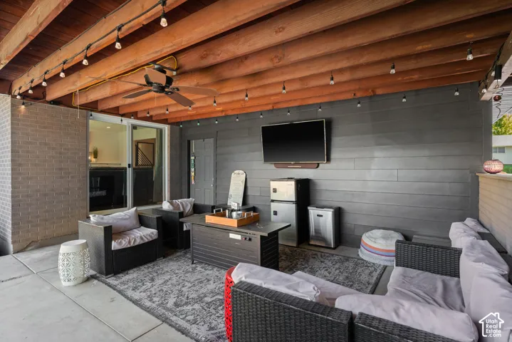 Modern outdoor living space featuring exposed wooden beam ceiling with recessed lighting, gray horizontal shiplap accent wall, and built-in entertainment setup with wall-mounted flat-screen television