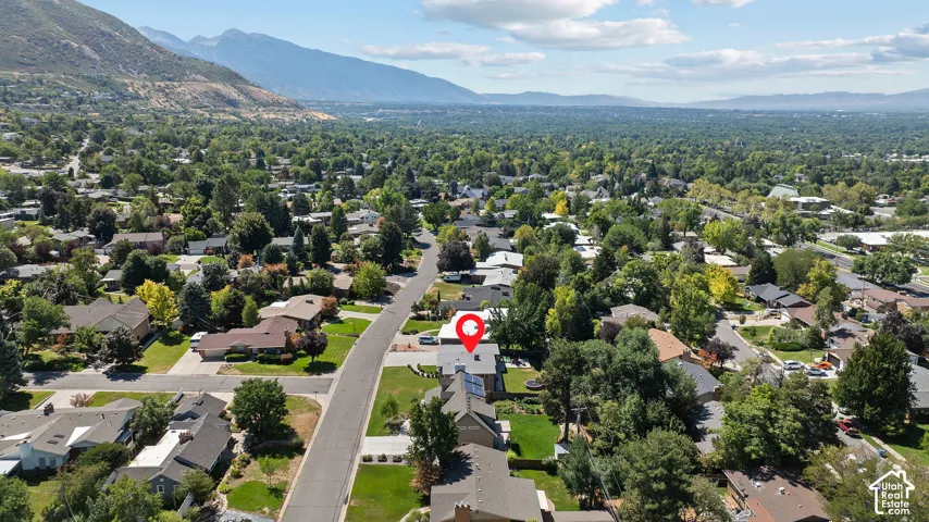 Aerial view showcasing this residential property situated on a tree-lined street within an established neighborhood, featuring mature landscaping, manicured lawn, and mountain backdrop