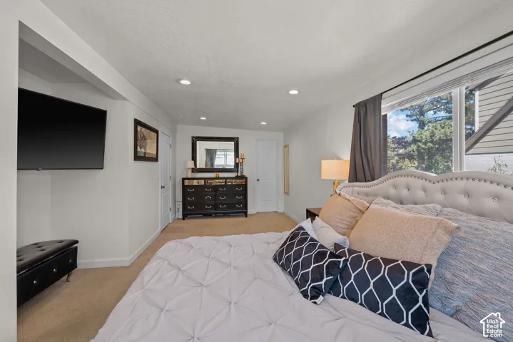 Primary Bedroom with Recessed Ceiling Lighting, Wall-Mounted Flat-Screen Television, Dark Wood Dresser with Attached Mirror, Tufted Upholstered Headboard, and Hardwood Flooring Throughout