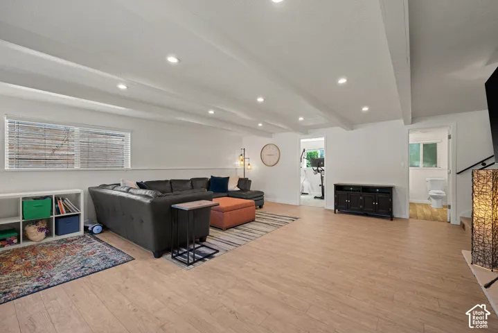 Spacious open-concept living area featuring wood-finish flooring throughout, recessed ceiling lighting, and large windows with plantation shutters