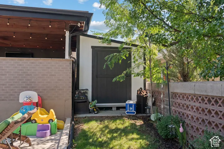 Covered patio with wood-finish ceiling, brick privacy wall, and string lighting