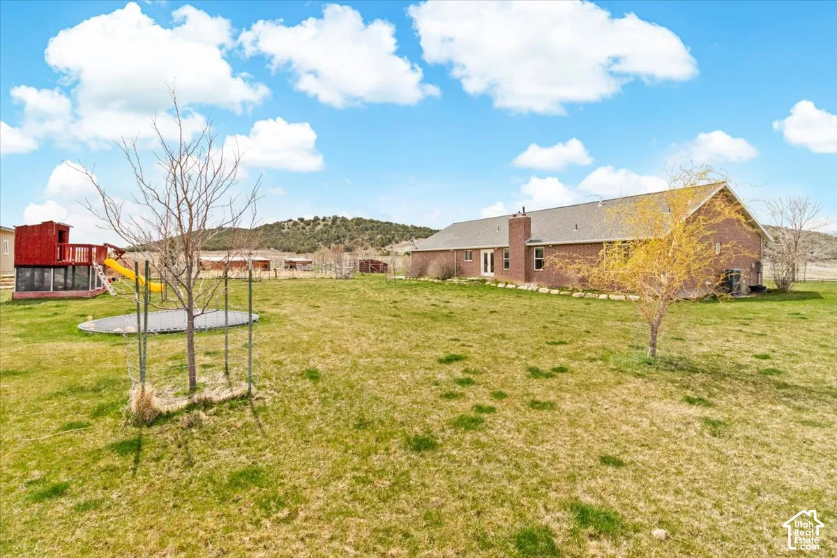 Expansive lawn backyard with a brick exterior residence, a wood stove chimney, and multiple mature trees