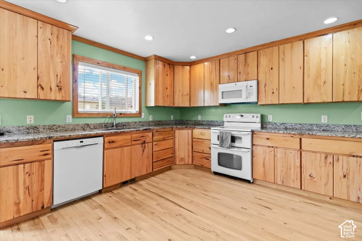 Kitchen featuring extensive wood cabinetry, light-toned wood flooring, light-colored countertops, white appliances, and recessed lighting