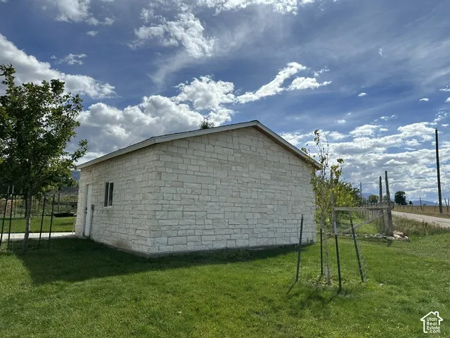 Stone-clad auxiliary building with a single window and door, situated on a grassy lot
