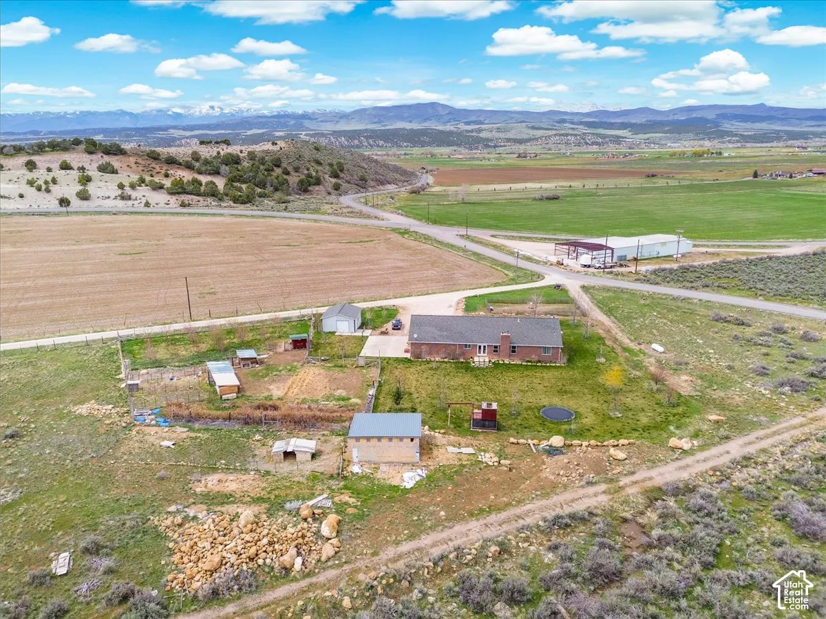 Expansive rural property featuring a brick residence, multiple outbuildings, gravel driveways, and distant mountain backdrops