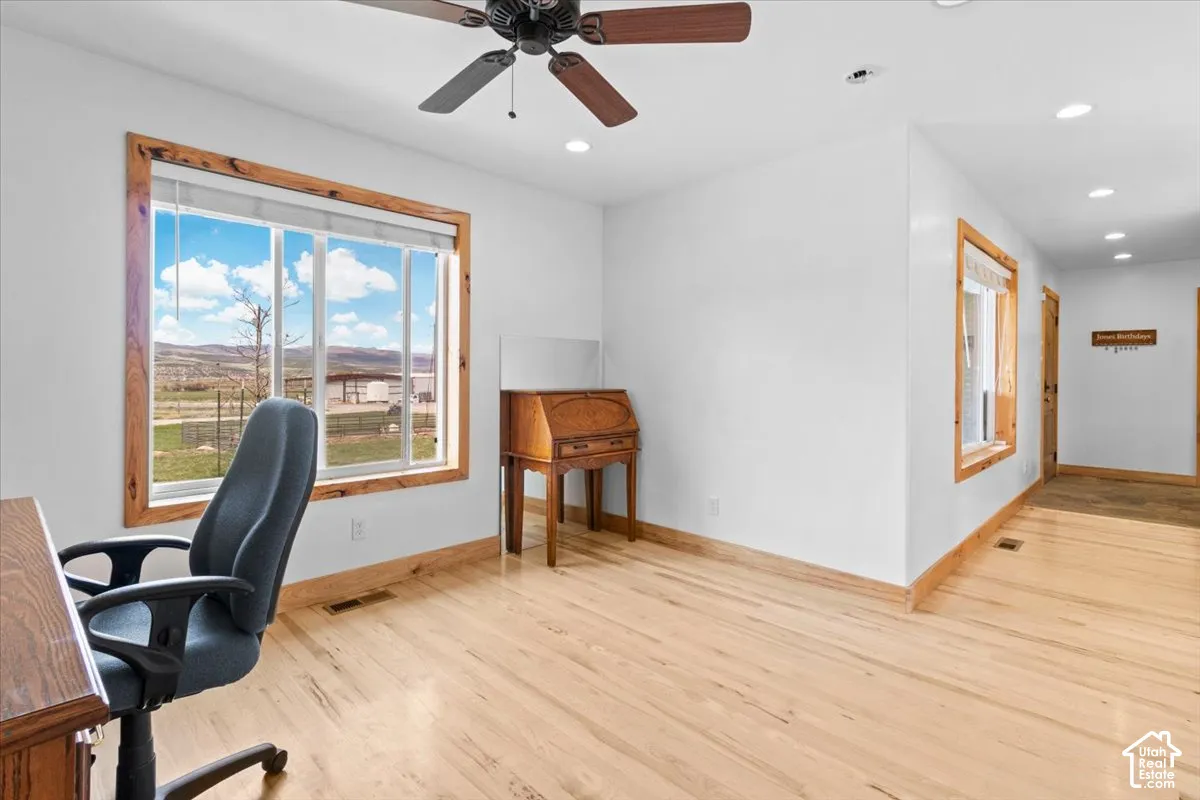 Bright office space featuring expansive windows with scenic countryside vistas, wood-finish flooring throughout, ceiling fan with integrated lighting, and recessed ceiling lights