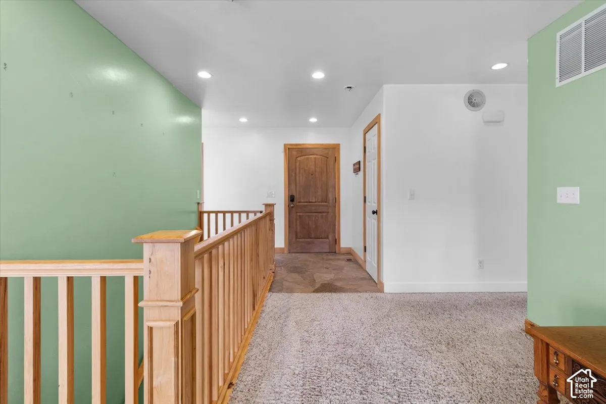 Light-toned wood railing with balusters, recessed lighting, wood-finish interior doors with dark hardware, and light carpet flooring