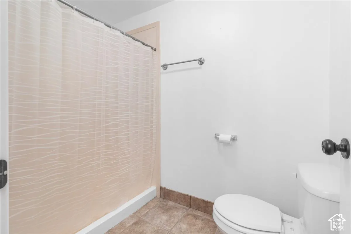 Tile flooring with coordinating tile base trim, white walls, and a white toilet