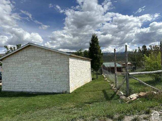 Stone-clad exterior, gabled roofline, established perimeter fencing, and distant mountain scenery
