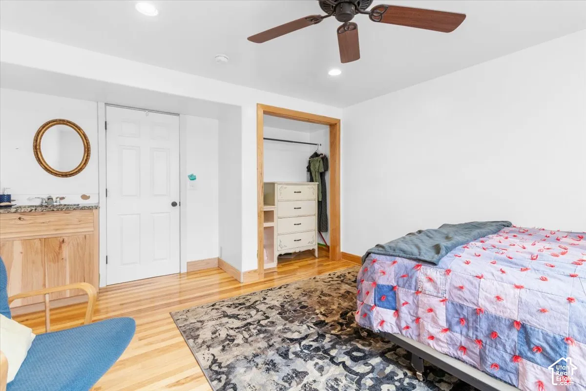 Wood-finish flooring, recessed lighting, ceiling fan, wood-toned door frame, and a built-in vanity with a stone countertop