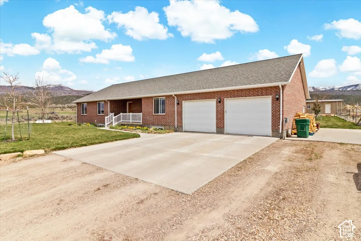 Brick exterior with a gray shingle roof, white railing at the entrance, two garage doors, and a concrete driveway