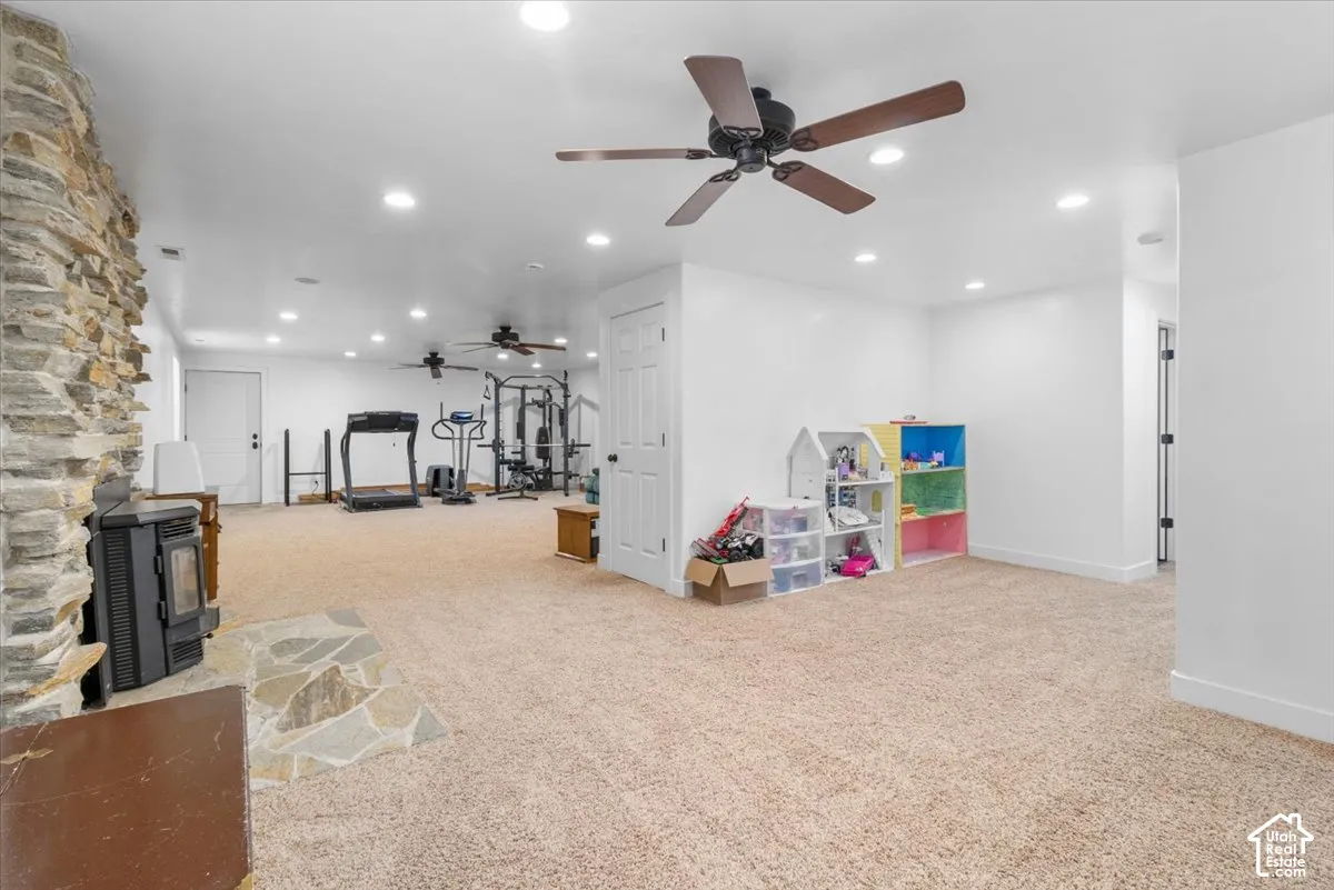 Expansive carpeted area featuring recessed lighting, ceiling fans, and a stone-clad wall with a hearth