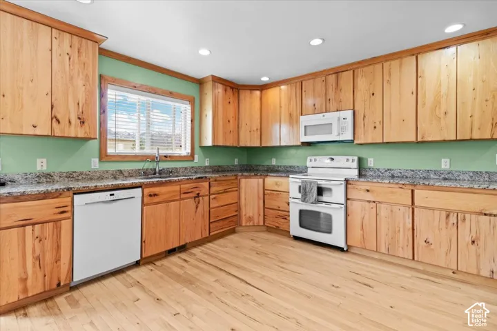 Kitchen featuring extensive wood cabinetry, light-toned wood flooring, light-colored countertops, white appliances, and recessed lighting