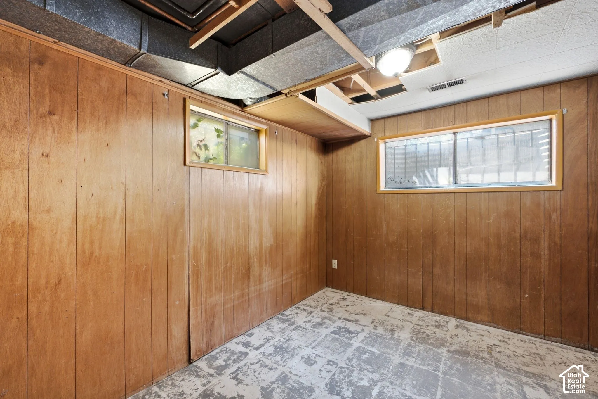 Paneled wall finish, exposed ceiling joists, two windows with wood trim, surface-mounted ceiling light fixture, concrete flooring